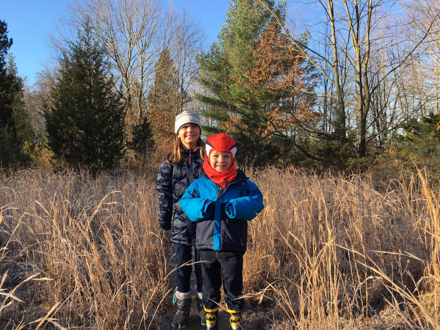 Two kids on one of their favorite trails in mid all, high wheat and trees in the background