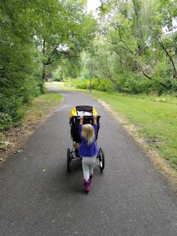 little girl pushing a stroller on a paved path