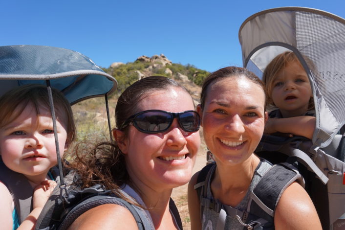 Hiking with a Hearing Loss by Vanessa Wright for Hike it Baby (image two moms with their daughters in hiking frame carriers, smiling at the camera)