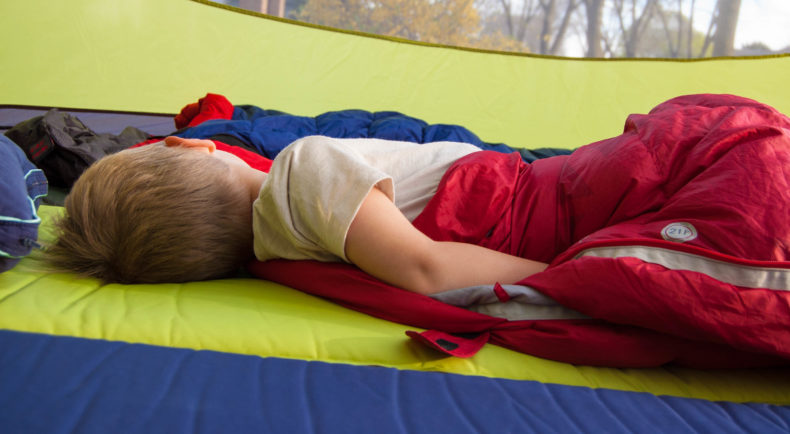 young boy sleeping in a tent with a red sleeping bag and a wool t-shirt