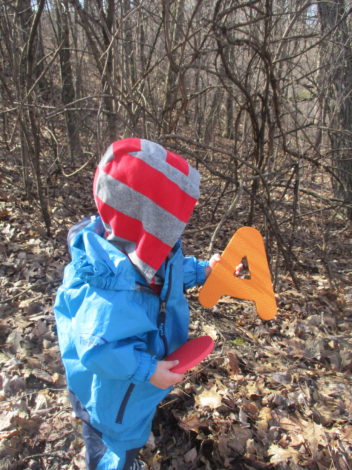 A is or Alphabet Themed Hikes by Moriah Butler for Hike it Baby (image of small child in a blue rain suit holding a foam letter A)