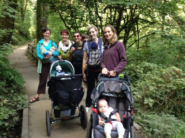 5 women, 5 babies and 2 strollers on a lush green nature path