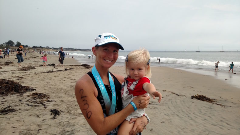 Mom and daughter on a beach after a race, mom wearing a finisher medal