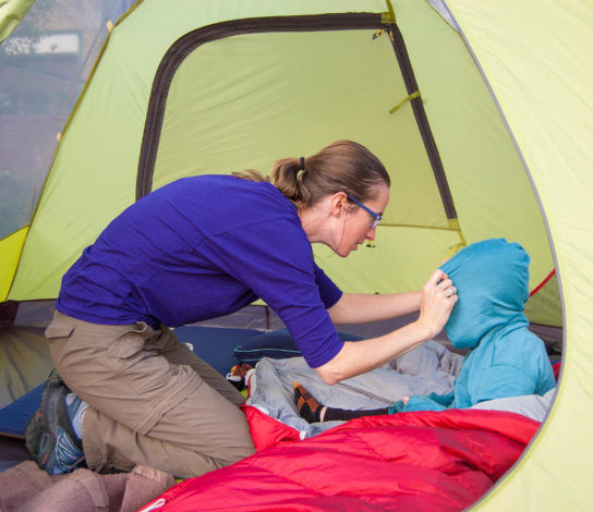 Mom adjusting the hood on a kid's hoodie while they sit in a tent