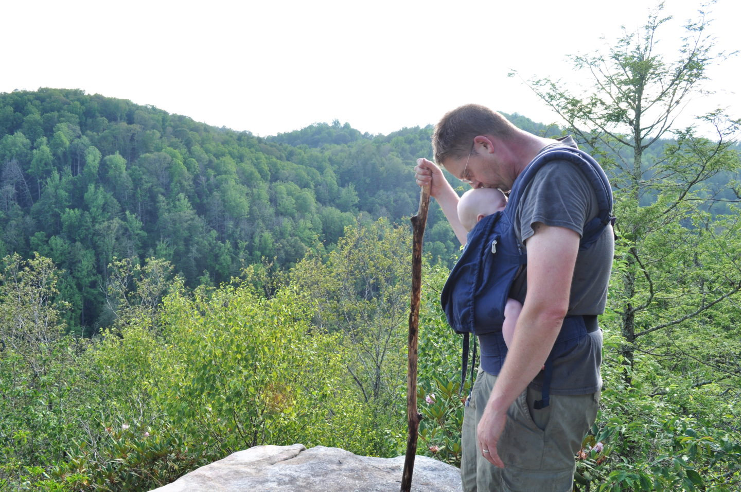 Dad kissing infant forehead with trees in the background