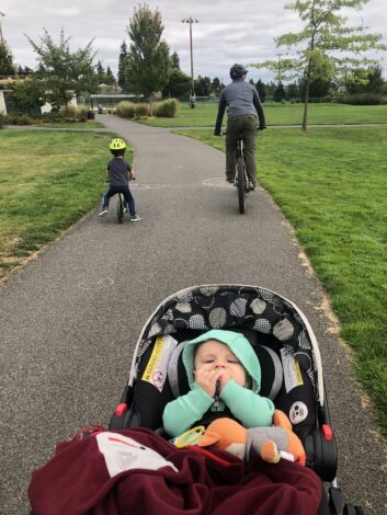 Parent and child riding bikes outdoors while baby is pushed in a stroller