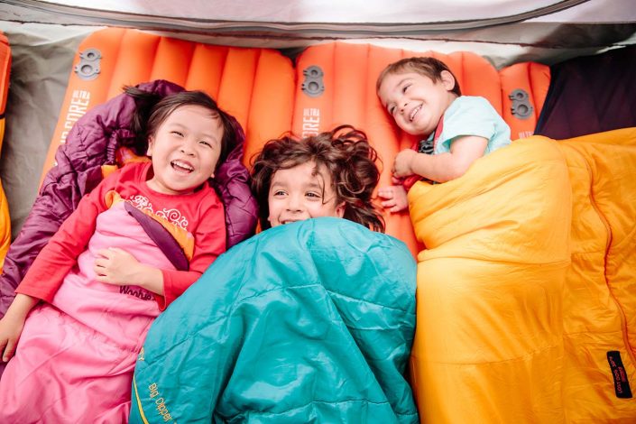 three young children in sleeping bags camping