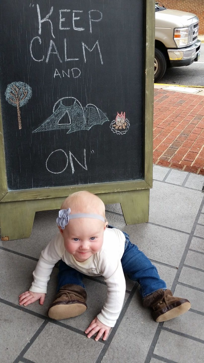 Infant in front of a "Keep Calm and Camp On" Sign.